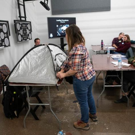 A woman zips up something that looks like a tent while students watch