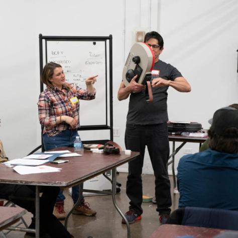 A man shows how a film loader feeds film into the camera while a woman explains