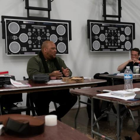 A man seated at a table explains something while another man listens intently