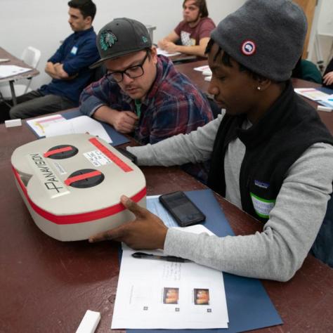 Seated student holding a film loader while another student watches